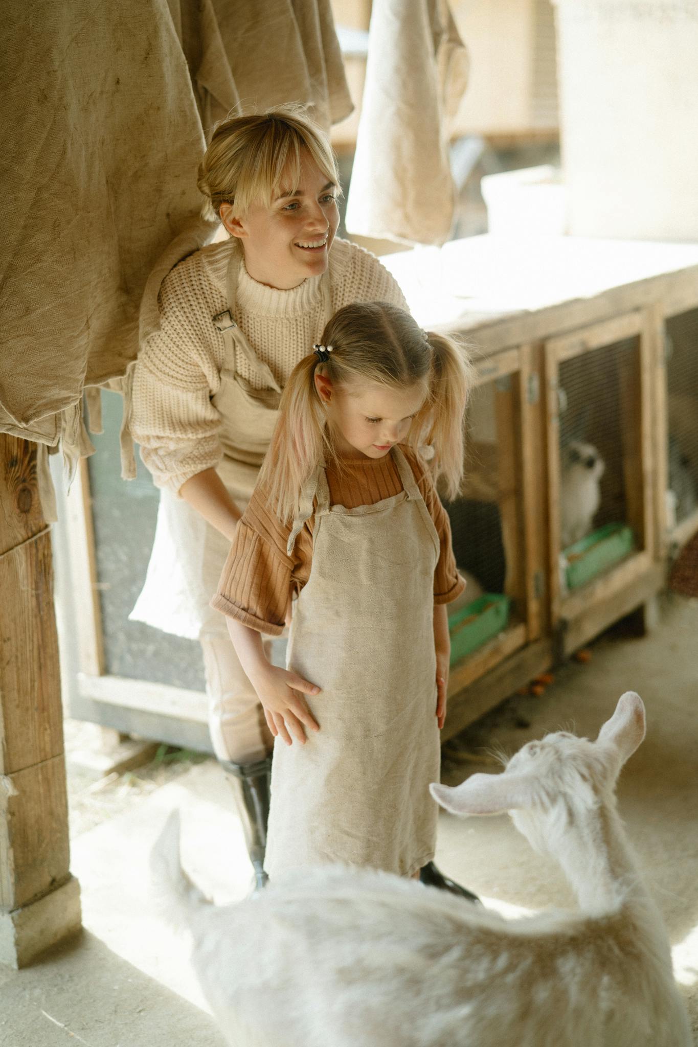 A mother and her daughter standing together in a goat pen, enjoying farm life.